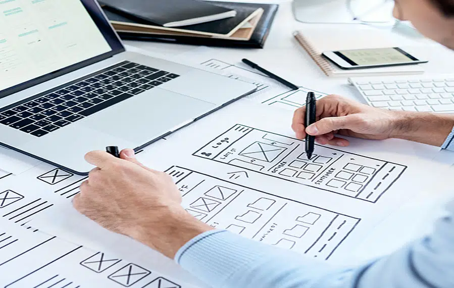 man creating a web design on paper, sitting in front of a laptop
